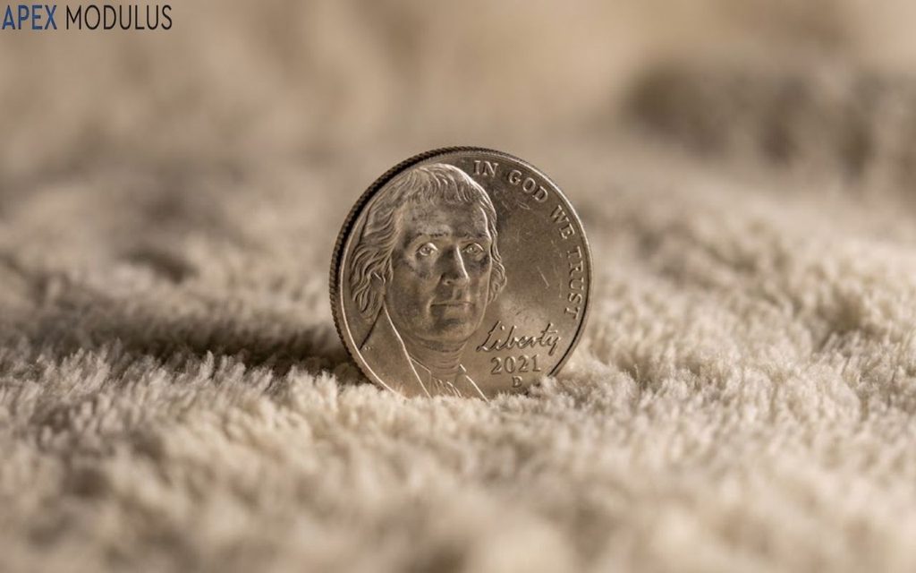 A macro, low-angle shot of a 2021 U.S. nickel standing upright on a soft, cream-colored textured fabric with a shallow depth of field.