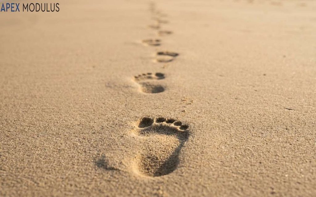 A line of bare footprints pressed into smooth sand, trailing straight into the soft-focus distance under warm late-afternoon light.