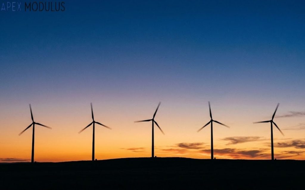 Five 300 feet wind turbines silhouetted against a gradient sunset sky on a dark hill.